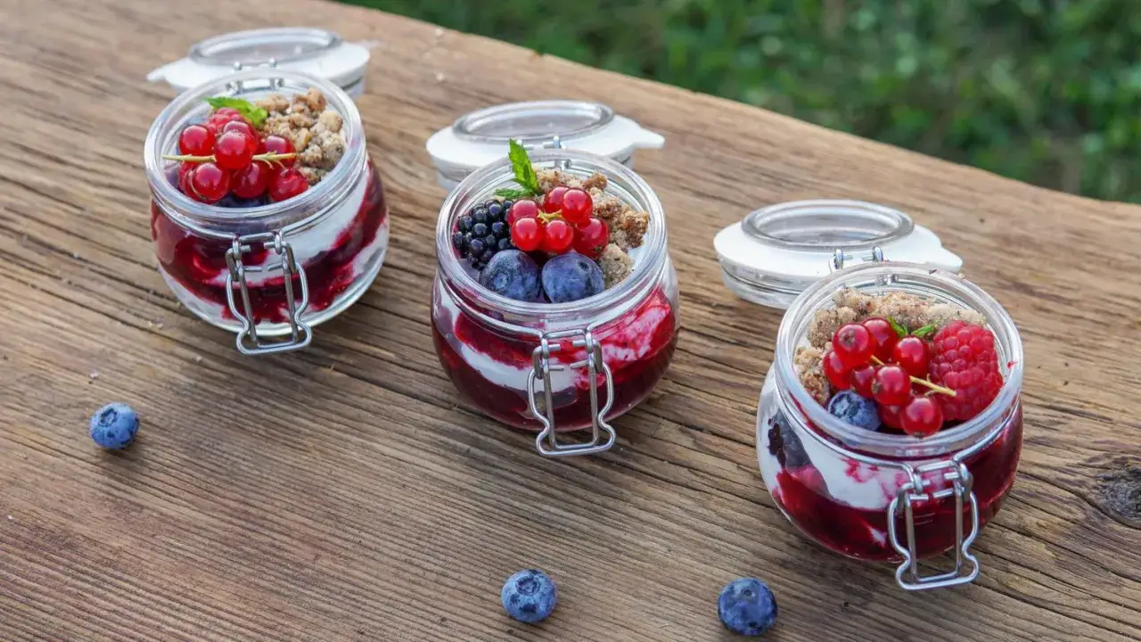 Deliziosa mousse allo yogurt con frutti di bosco e crumble in barattoli di vetro, su un tavolo di legno rustico.