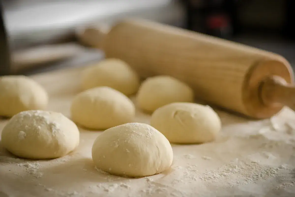 Impasti lievitati pronti per essere lavorati, con un mattarello sullo sfondo. Il bicarbonato nei dolci serve a renderli soffici e leggeri.