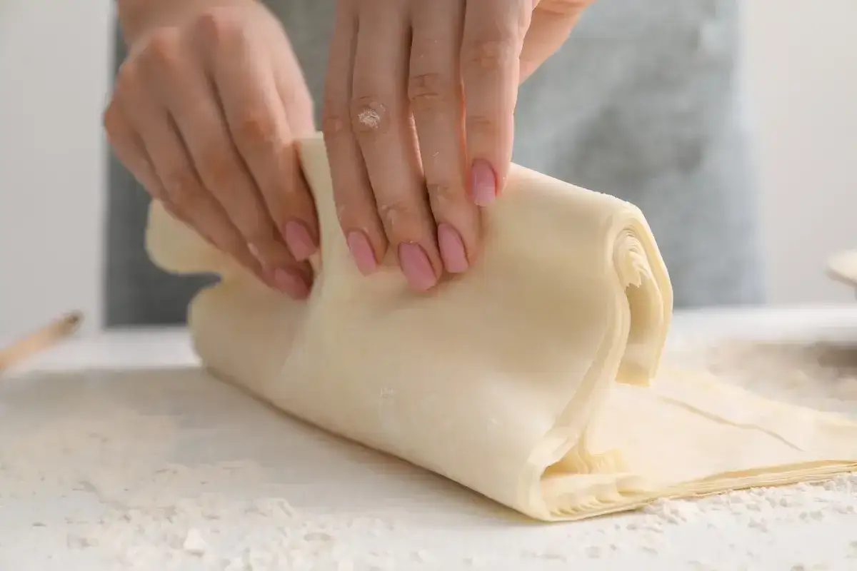 Mani che lavorano la pasta fillo, uno degli ingredienti base per dolci e salati croccanti.