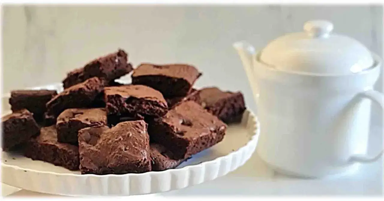 Brownies ricetta: tanti quadratini di cioccolato su un piatto bianco, accanto a una teiera.