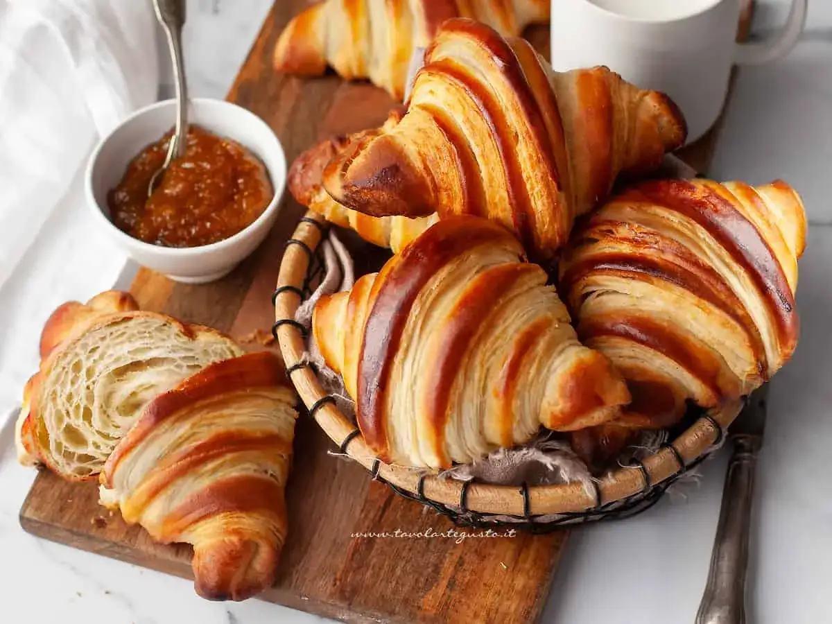 Croissant Francia dorati e fragranti, uno tagliato a met&agrave; per mostrare la sfogliatura perfetta, accompagnati da marmellata.