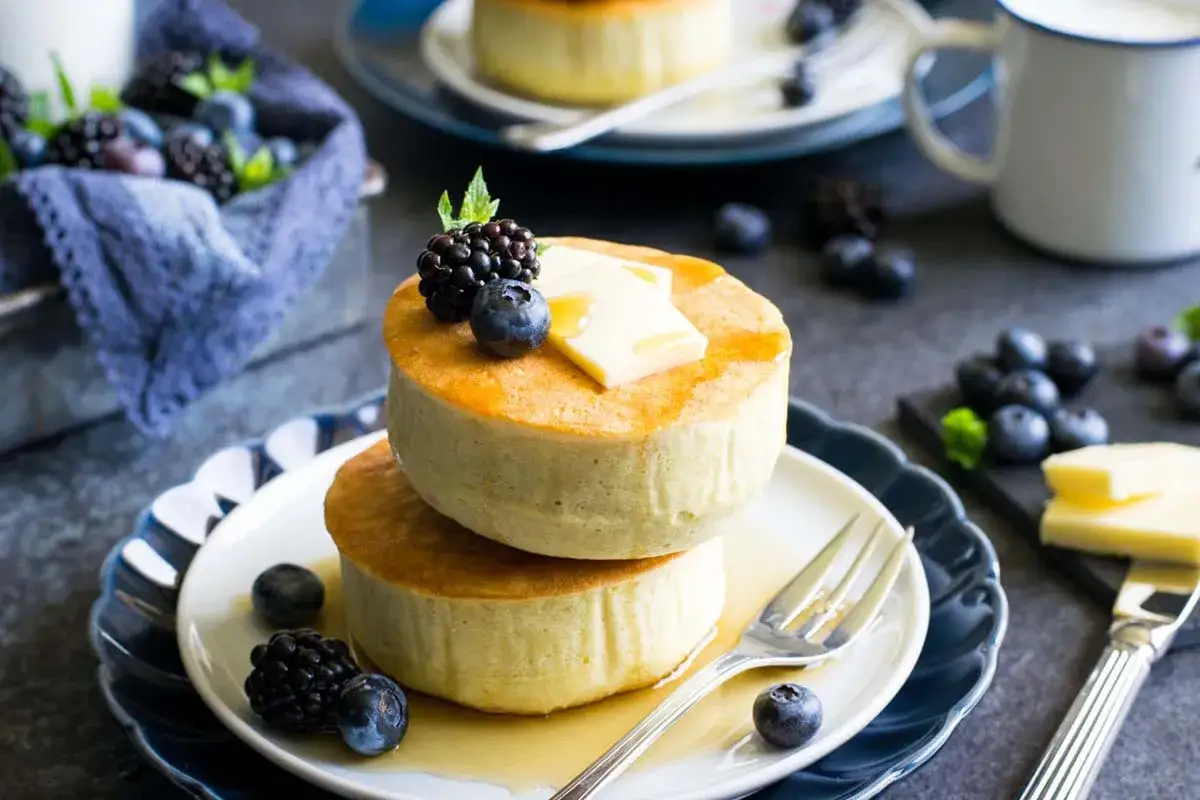 Deliziosi pancake giapponesi soffici, impilati e guarniti con frutti di bosco, burro e sciroppo.
