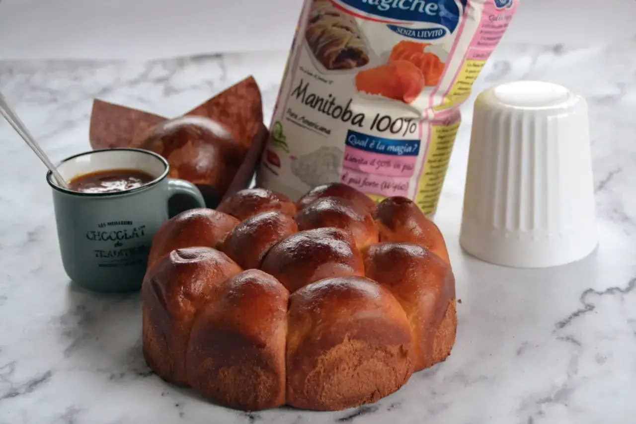 Dolci soffici e dorati, perfetti per la colazione, preparati con farina Manitoba. Accanto, una tazza di cioccolata calda e un sacchetto di farina.