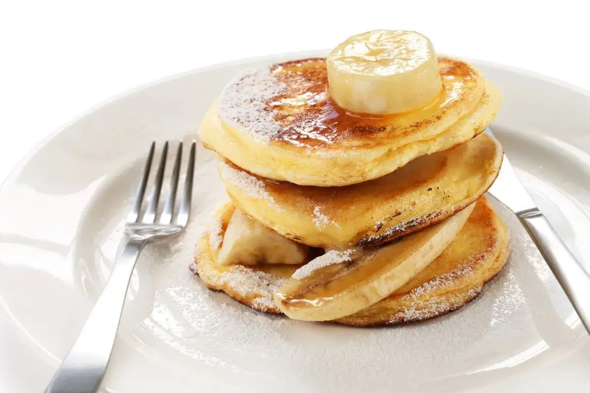 Pancake con albumi soffici, guarniti con sciroppo d'acero, zucchero a velo e fette di banana.