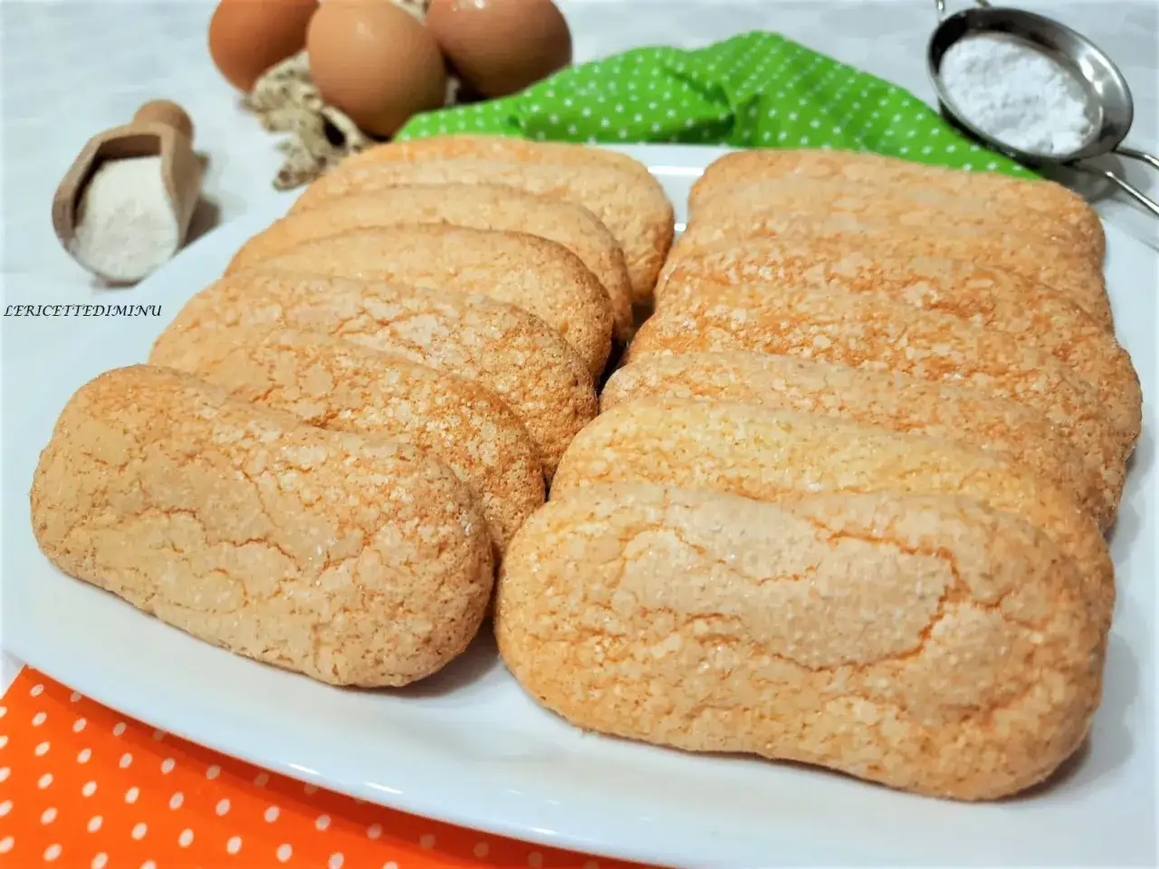 Savoiardi fatti in casa dorati e friabili, pronti per il tiramisù. Ingredienti freschi sullo sfondo.