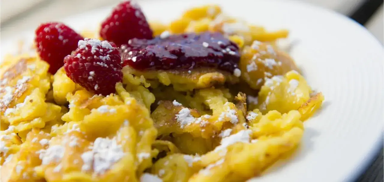 Frittata dolce tirolese, un piatto goloso con lamponi freschi e marmellata, spolverato di zucchero a velo.