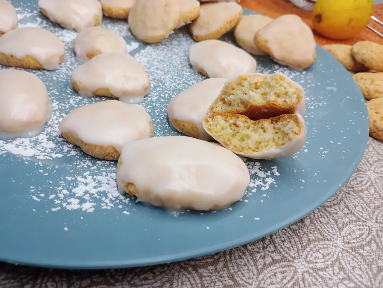 Biscotti al limone glassati, uno spezzato rivela un interno soffice e profumato. Un limone fresco sullo sfondo.