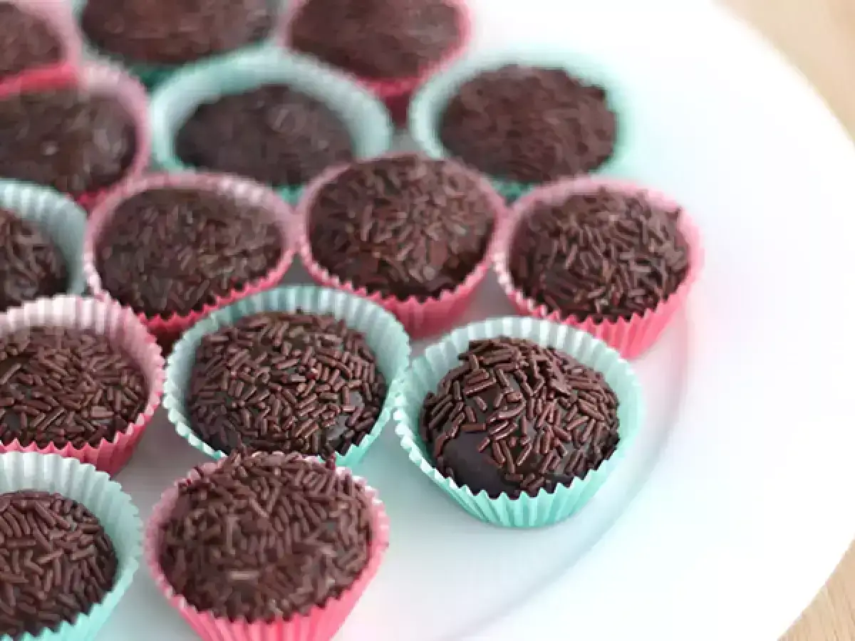 Deliziosi dolcetti brasiliani ricoperti di codette di cioccolato, presentati in pirottini colorati su un piatto bianco.