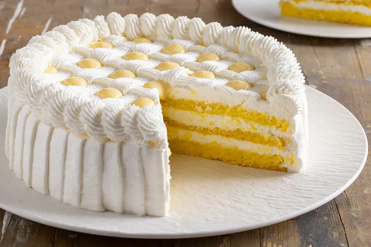 Torta soffice con strati di pan di spagna giallo e crema solida per farcire torte, decorata con panna montata e gocce gialle.