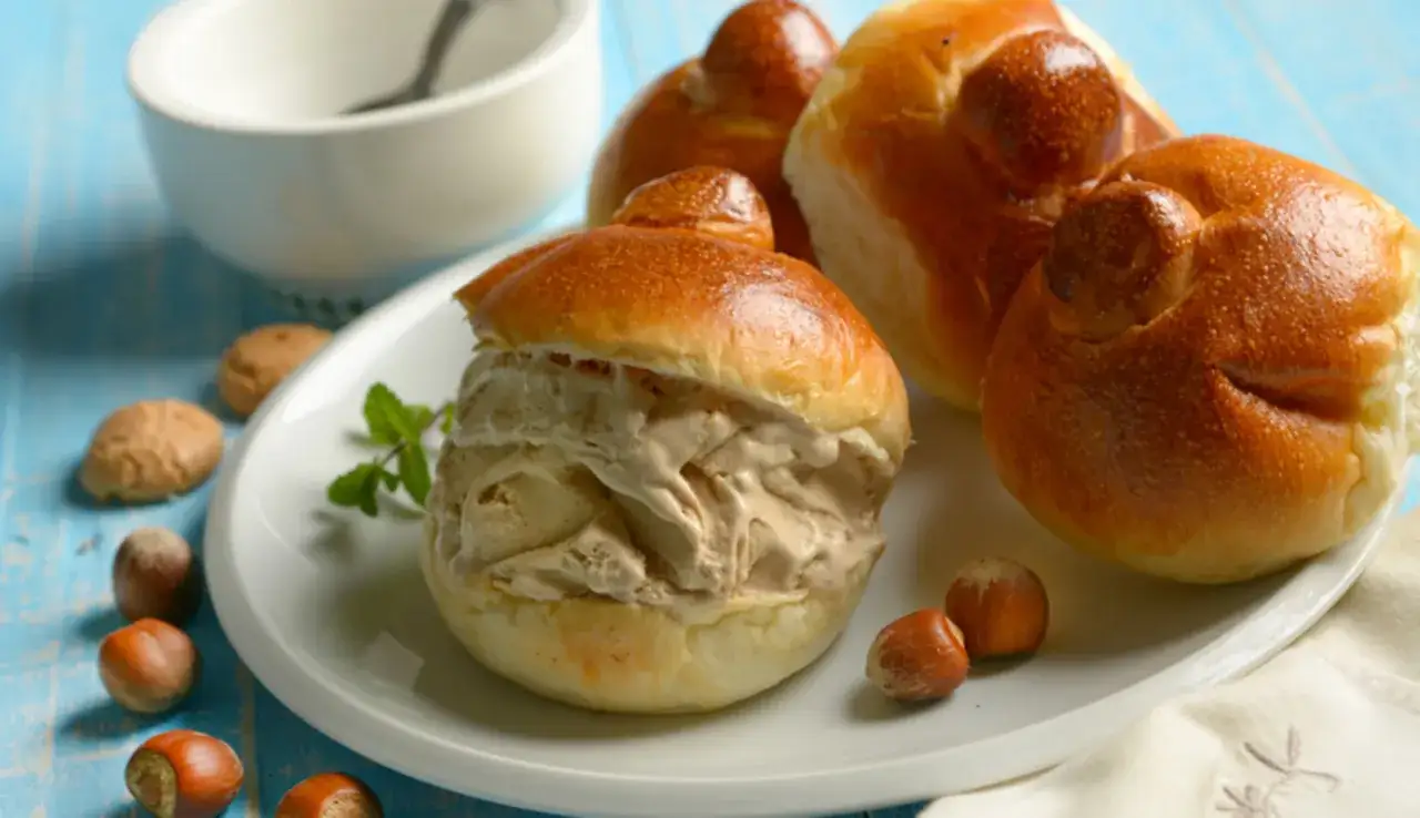 Brioches col tuppo, soffici e dorate, ripiene di gelato cremoso. Un dolce siciliano da gustare con nocciole e menta.