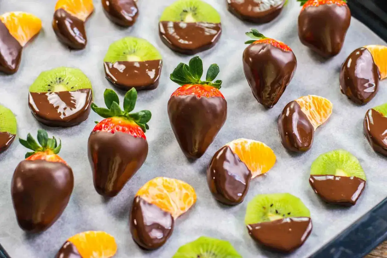 Fragole, spicchi di mandarino e fette di kiwi immerse nel cioccolato fondente, un delizioso assortimento di frutta al cioccolato.