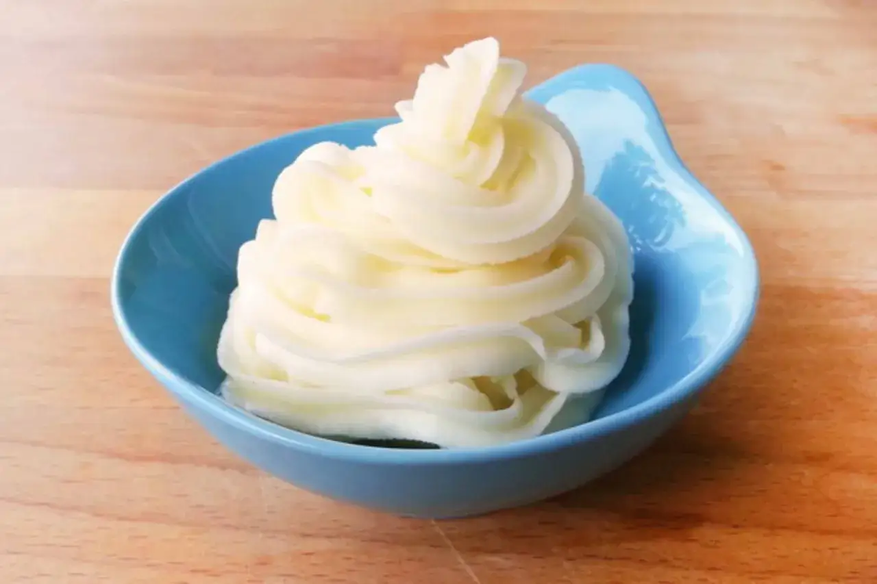 Pur&egrave; di patate a pomata, servito in una ciotola blu su un tagliere di legno.