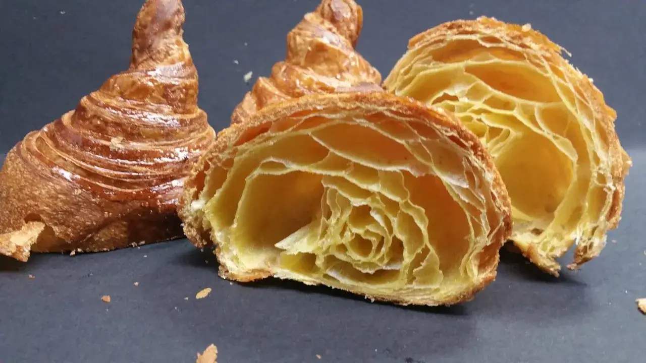I croissant dorati e sfogliati, uno intero e due tagliati a metà, rivelano la loro struttura alveolata e friabile.