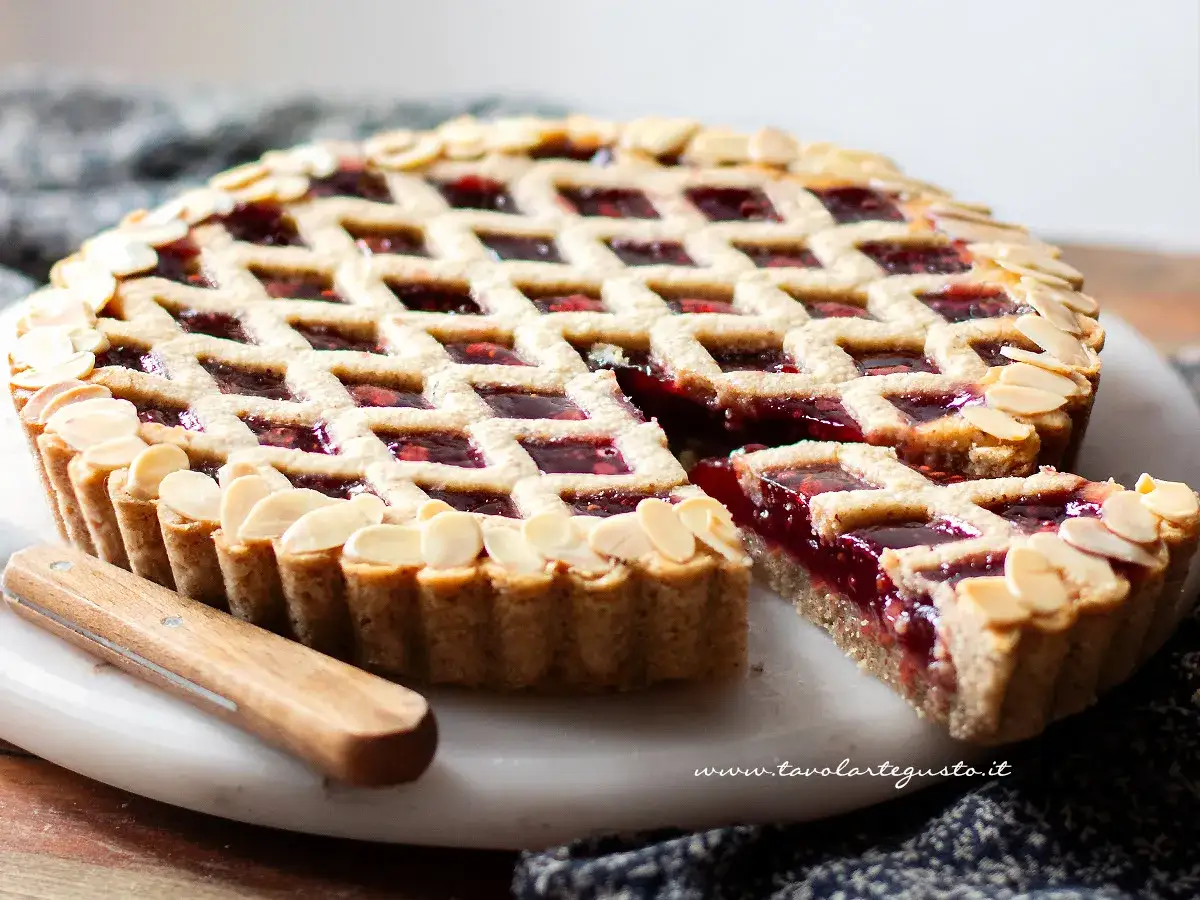 Torta Linzer ricetta originale: crostata con marmellata di frutti rossi, decorata con mandorle a lamelle e una griglia di pasta frolla.