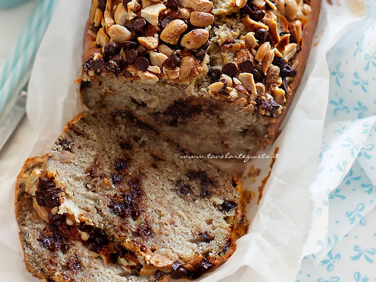 Fetta di banana bread con gocce di cioccolato e noci, ricoperta da mandorle e nocciole tostate.