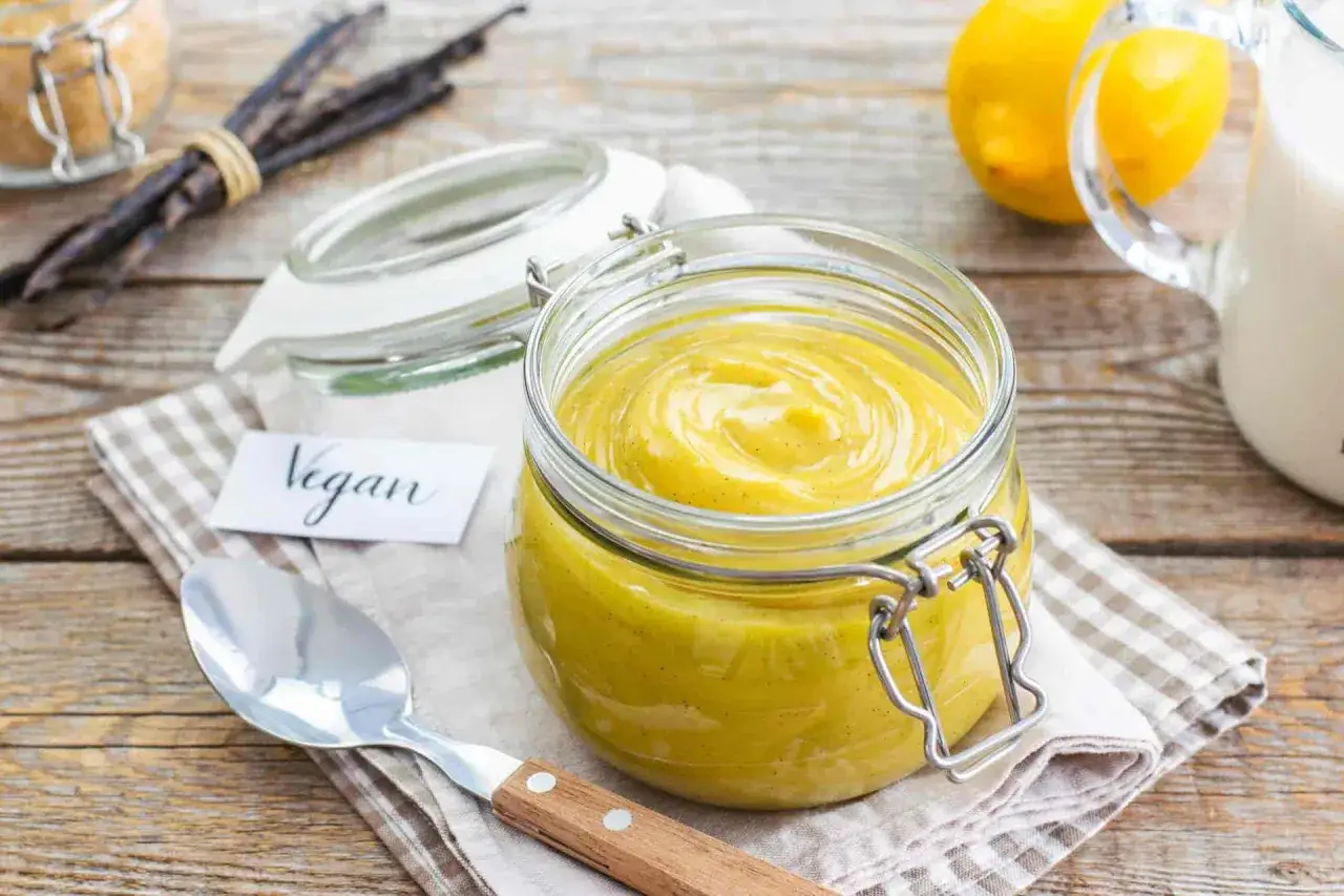 Crema pasticcera vegana in un barattolo di vetro, con bacche di vaniglia e limoni sullo sfondo.