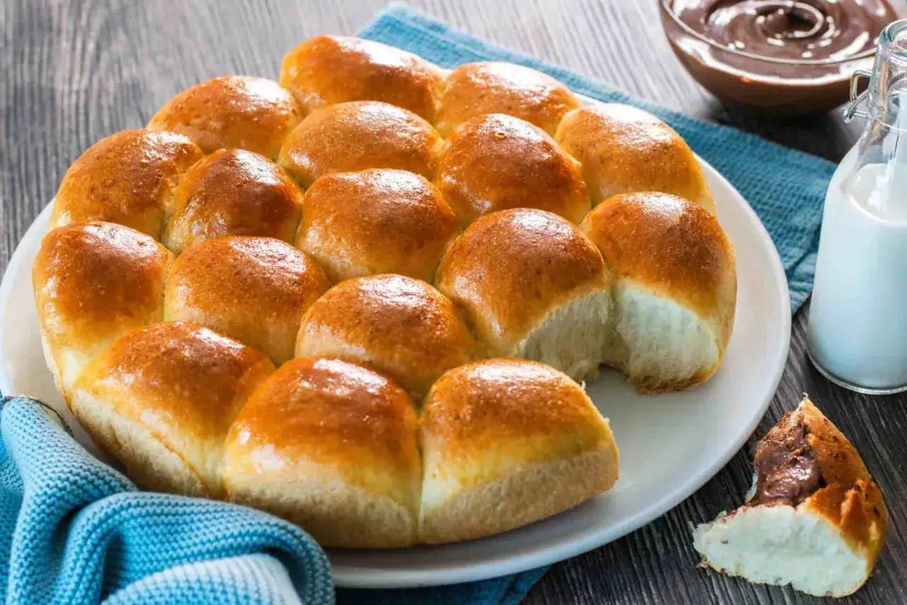 Deliziosi dolci lievitati dorati su un piatto bianco, pronti per essere gustati con crema al cioccolato e latte.