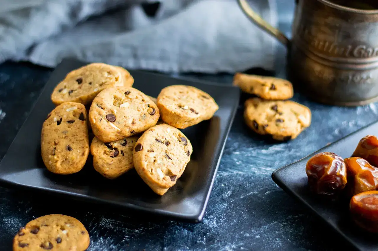 Biscotti vegan con gocce di cioccolato e datteri su piatti neri, pronti per essere gustati.