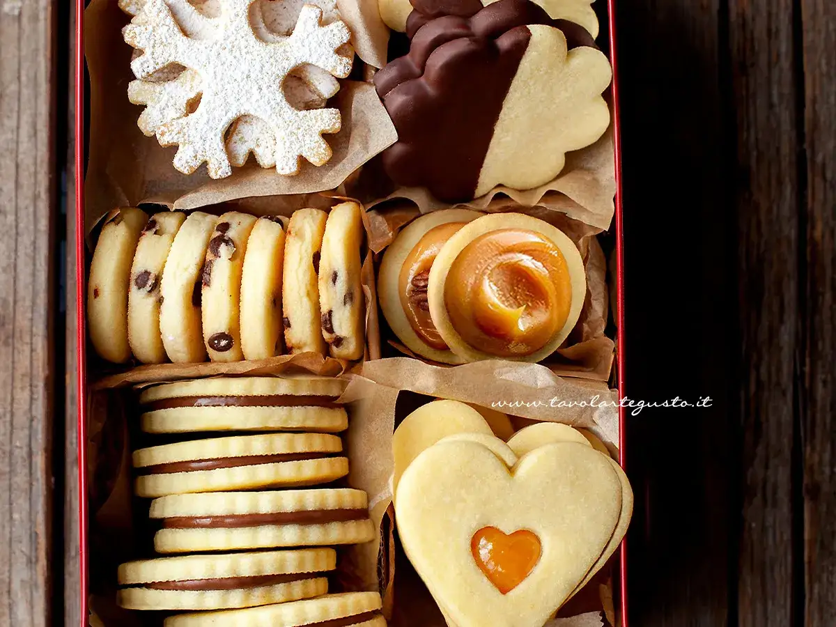 Scatola piena di biscotti al burro: a fiocco di neve, con gocce di cioccolato, ripieni di caramello e a forma di cuore.