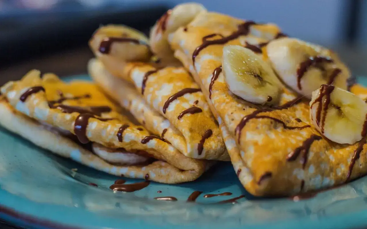 Crepes arrotolate con banana e cioccolato fuso, ingredienti semplici per un dolce delizioso.