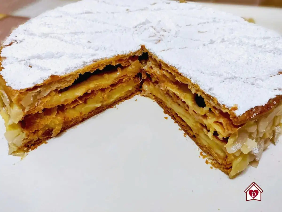 Un delizioso millefoglie alla crema, con strati croccanti di pasta sfoglia e una ricca crema pasticcera, cosparso di zucchero a velo e mandorle.