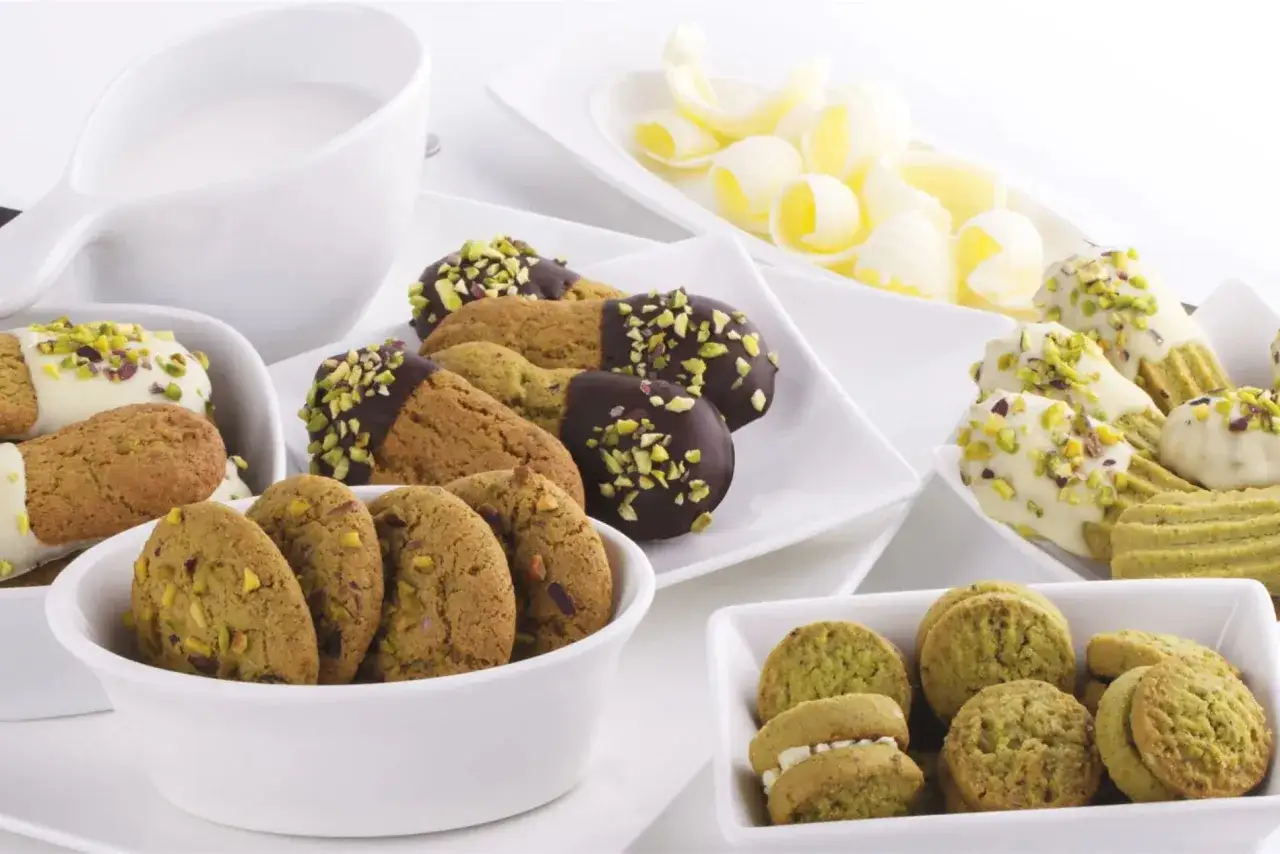 Varietà di tipi di biscotti, alcuni ricoperti di cioccolato fondente e pistacchi, altri di cioccolato bianco e pistacchi, e altri ancora con ripieno di crema.