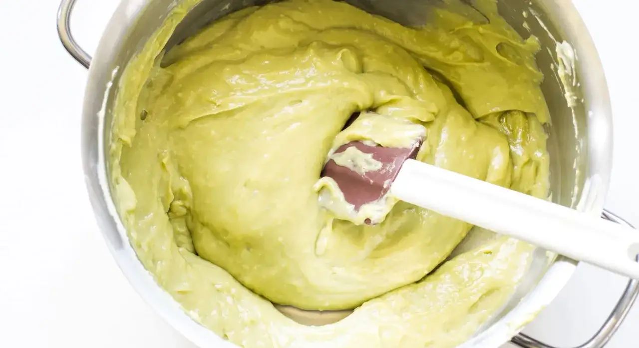 Crema di pistacchio ricetta: una spatola mescola un composto verde chiaro e cremoso in una ciotola d'acciaio.