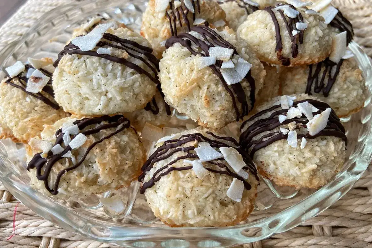 Deliziosi dolcetti al cocco, ricoperti di cioccolato fondente e scaglie di cocco croccante, su un piatto di vetro.