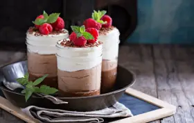 Tre deliziosi bicchierini di dolce freddo al cioccolato e panna, guarniti con lamponi freschi e scaglie di cioccolato.