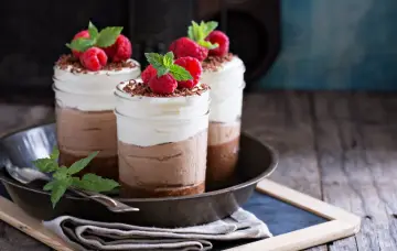 Tre deliziosi bicchierini di dolce freddo al cioccolato e panna, guarniti con lamponi freschi e scaglie di cioccolato.