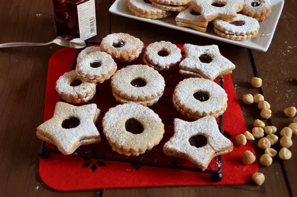 Deliziosi biscotti Linzer, a forma di stella e tondi, ripieni di marmellata e spolverati di zucchero a velo, su una griglia nera.